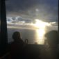 Two people sitting on a window ledge looking out at the ocean.