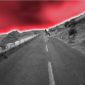 A black and white photo of a road with red sky in the background.